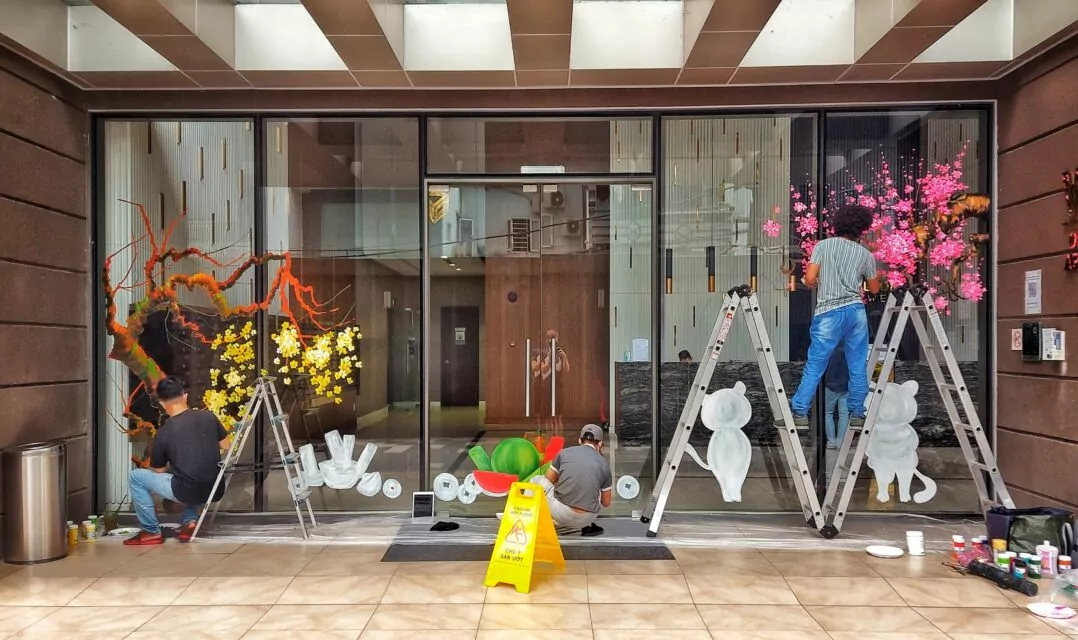 Artists paint the glass wall of the Wilton Tower lobby with flowers, fruits, and lucky symbols to celebrate Tết, the Vietnamese New Year.