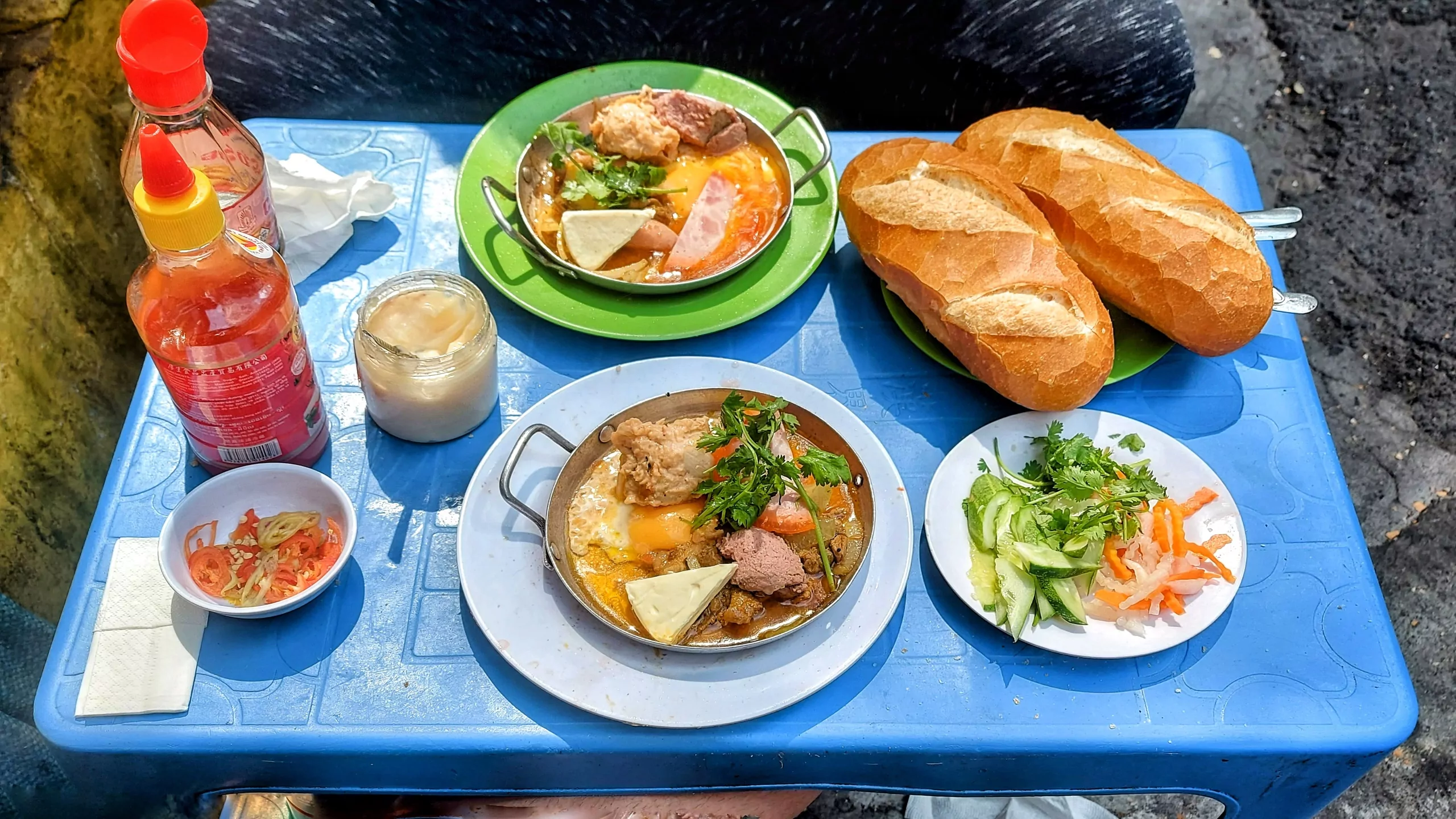Bánh mì chảo, a classic and very hearty breakfast served in a hot pan with fried egg, cheese, sliced and spread sausages, various vegetables, and crispy bánh mì for topping and dipping. What a way to start a day. Price: 50,000 VNĐ (≈1.99 EUR).