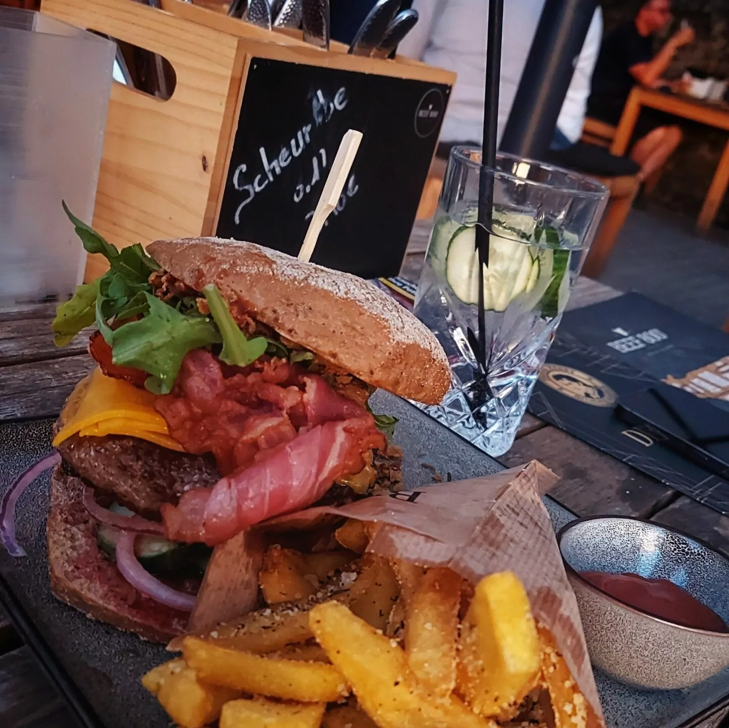 Huge classic bacon cheeseburger from Beef 800° in Würzburg with juicy beef, crispy bacon, tender cheddar, fresh arugula, onions and tomatoes, and spicy sauces. Served with hearty Grana Padano and rosemary fries, along with one or two, or even three gin and tonics. Or four. Price: 13,50 + 4,90 EUR.