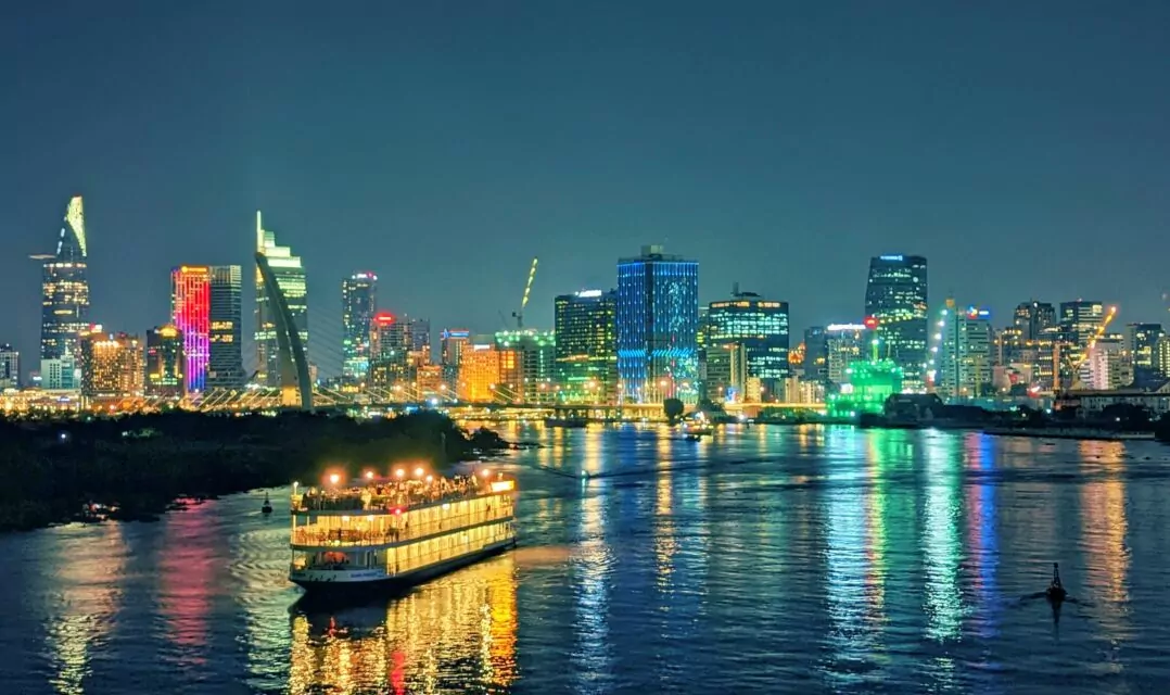 The night skyline of Sài Gòn's District 1, shining with bright colors from countless LEDs and spotlights and adding beautiful reflections on the dark waters of the Sài Gòn River. While I was taking the picture, a party boat was passing by with freaking Vinahouse.