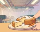 A wooden serving board held out toward the viewer with a round golden carrot cake on it, one wedge cut out showing the orange-flecked crumb, an open-plan office with concrete ceiling and ducts behind